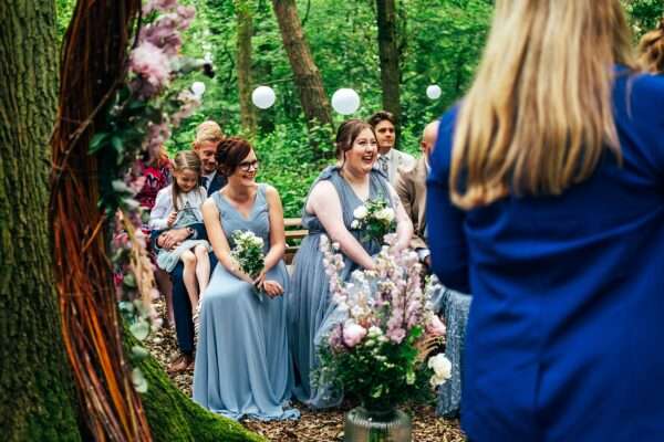 Bridesmaids in cornflower blue laugh during woodland ceremony at Captains Wood Barn