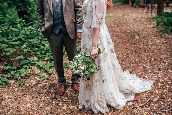 Bride in House of Savin gown holds wildflower bouquet with Groom in brown tweed at Captains Wood Barn