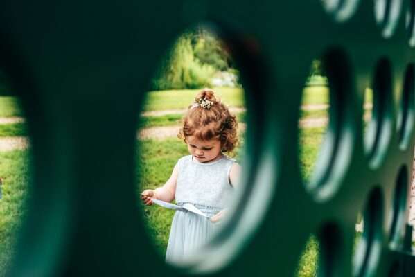 Flower girl plays with dress through the circle hole in giant connect 4 at Captains Wood Barn