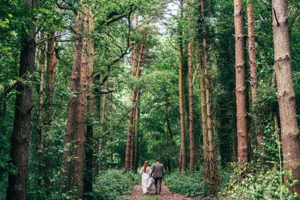 Bride and Groom walk through really tall trees at Captains Wood Barn