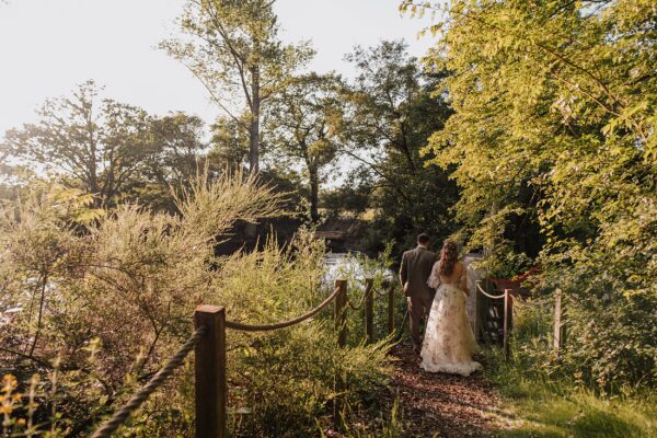 Bride and Groom walk to bridge over pond at sunset at Captains Wood Barn