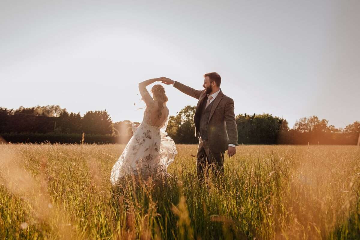 Bride and Groom dance in long grass at sunset at Captains Wood Barn