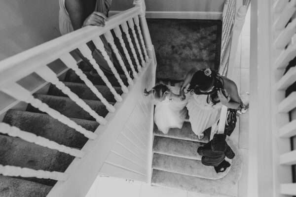 Bridesmaid helps flower girl down the stairs during prep