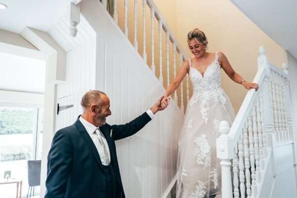 Father of the bride helps bride down the stairs on wedding morning