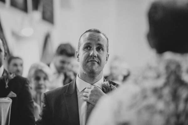 Groom adjusts tie as he waits for entrance of the bride in church