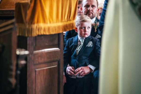 page boy looks grumpy during wedding ceremony in church