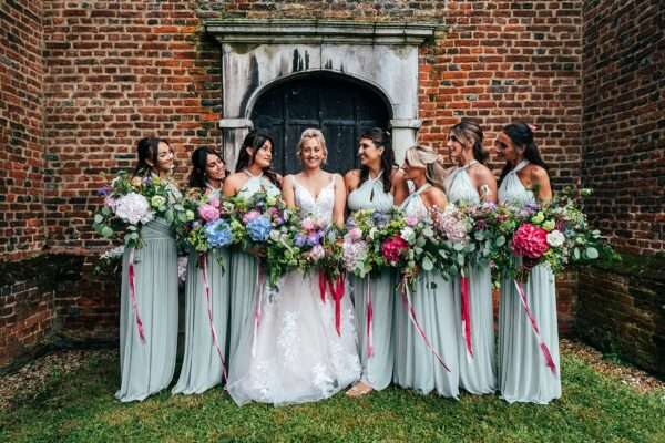 Bridesmaids and Bride hold oversized wild bouquets outside Essex church