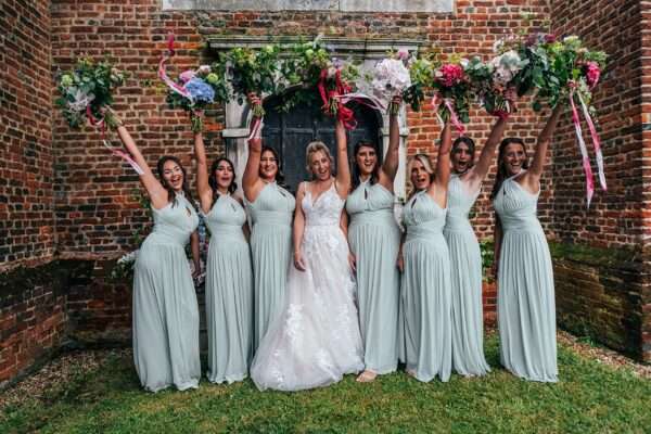 Bride and Bridesmaids wave oversized wild hand tied bouquets outside Essex church