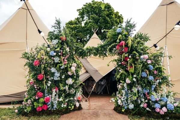 Huge summer bright floral arch at entrance to tipi for an Essex back garden wedding