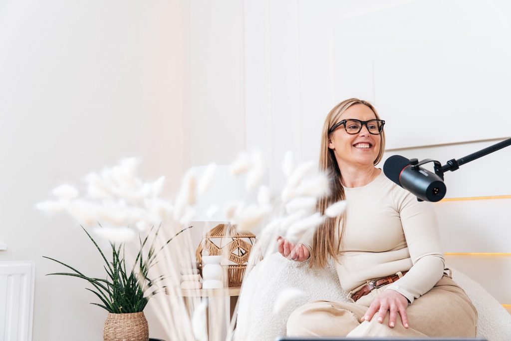 Essex Branding, Content and Head Shot photographer Woman in cream sits on chair and talks into mic for podcast