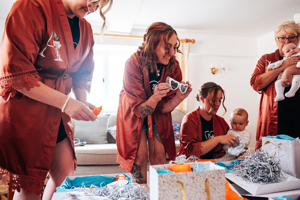 bridesmaids in copper dressing gowns hold up heart shaped sunglasses as they open gifts
