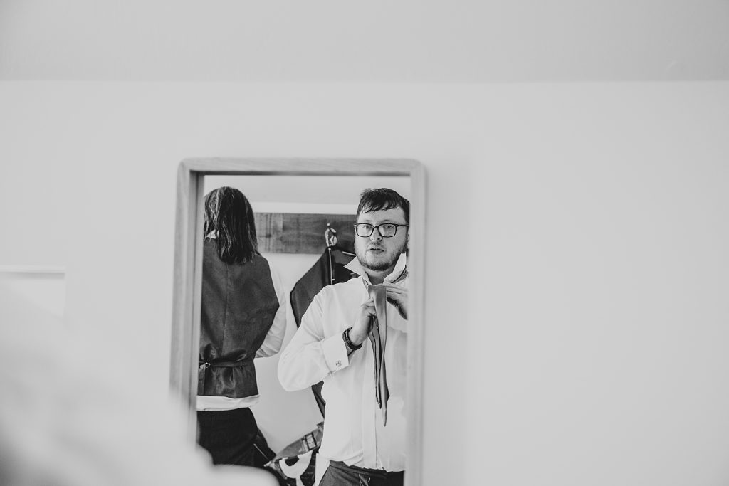 reflection of Groom doing up tie in mirror