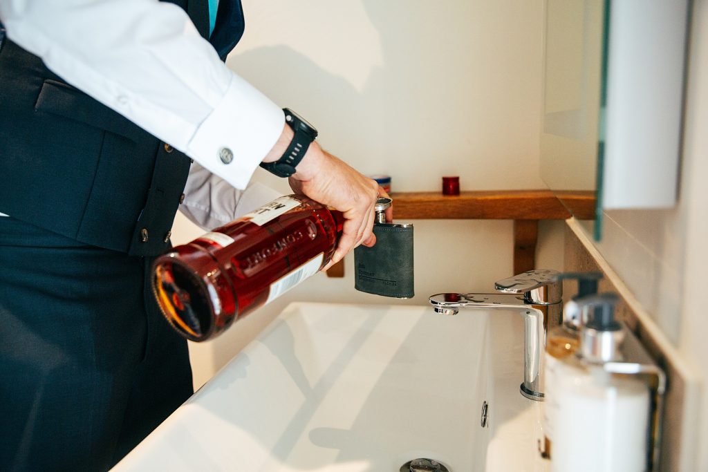 Best man pours whisky into hip flask