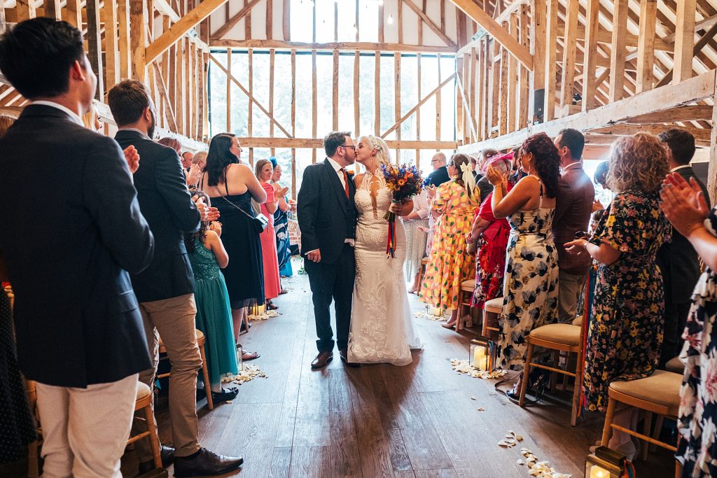 bride and groom stop to kiss on walk down aisle