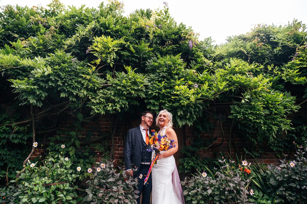 bride and groom laugh as they stand under wisteria canopy in walled gardens