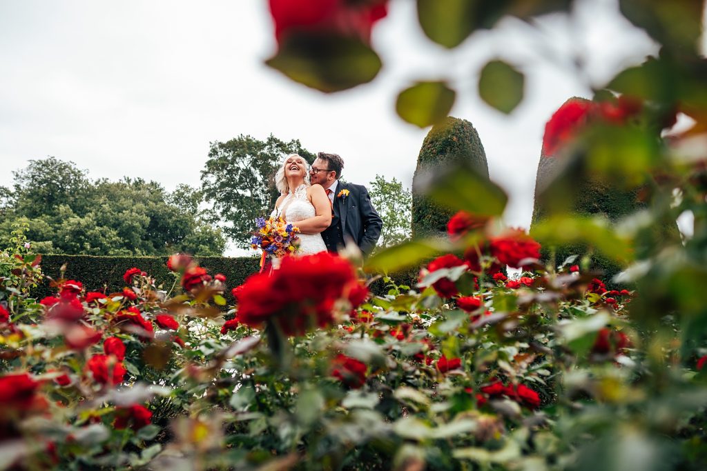 bride and groom laugh in red rose garden