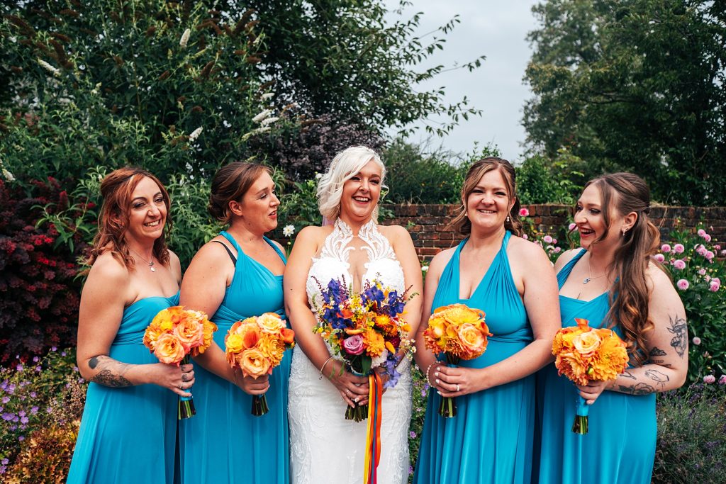 bride with bridesmaids in turquoise hold orange bouquets