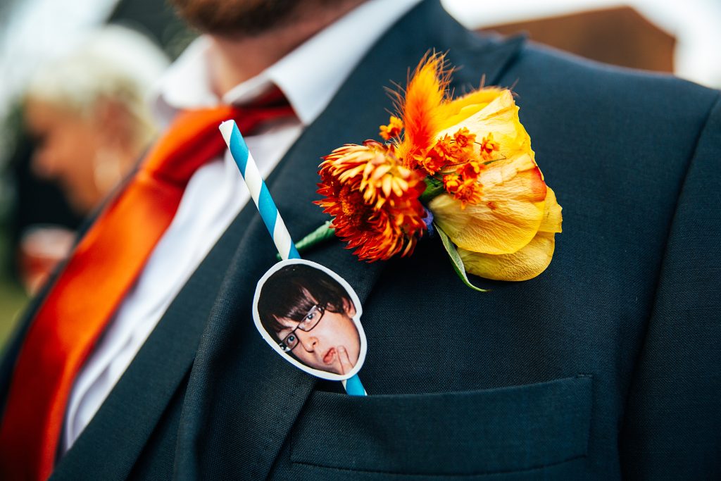 close up of button hole on best mans jacket with straw and groom's head