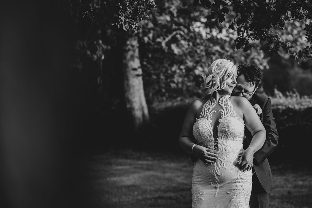 groom kisses bride on shoulder in gardens