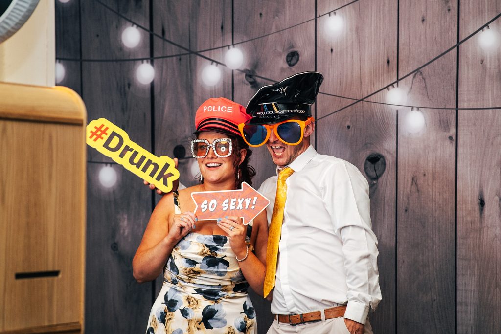 laughing guests in glasses and hats in photo booth