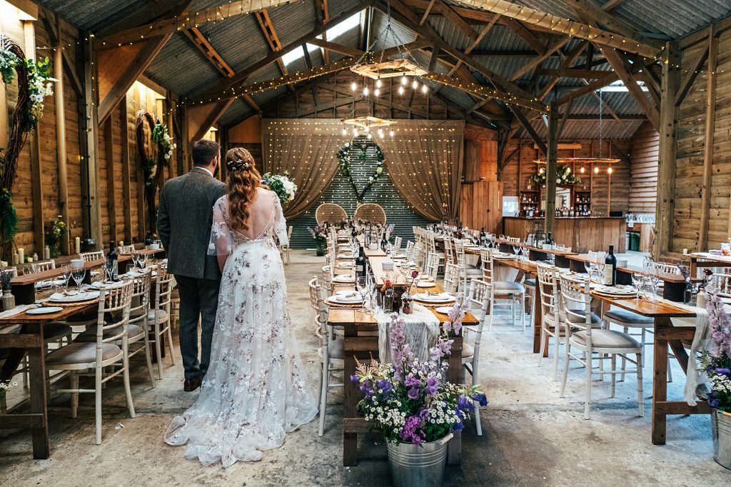 bride and groom with backs to the camera stand and admire the room set up for their wedding breakfast