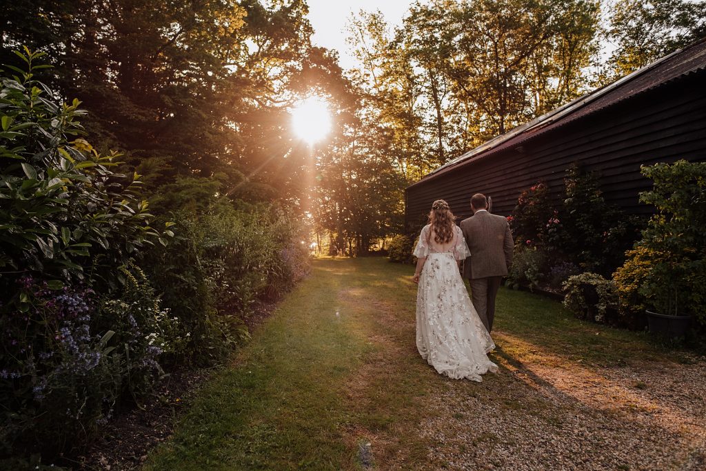 bride and groom walk past a barn towards the setting sun