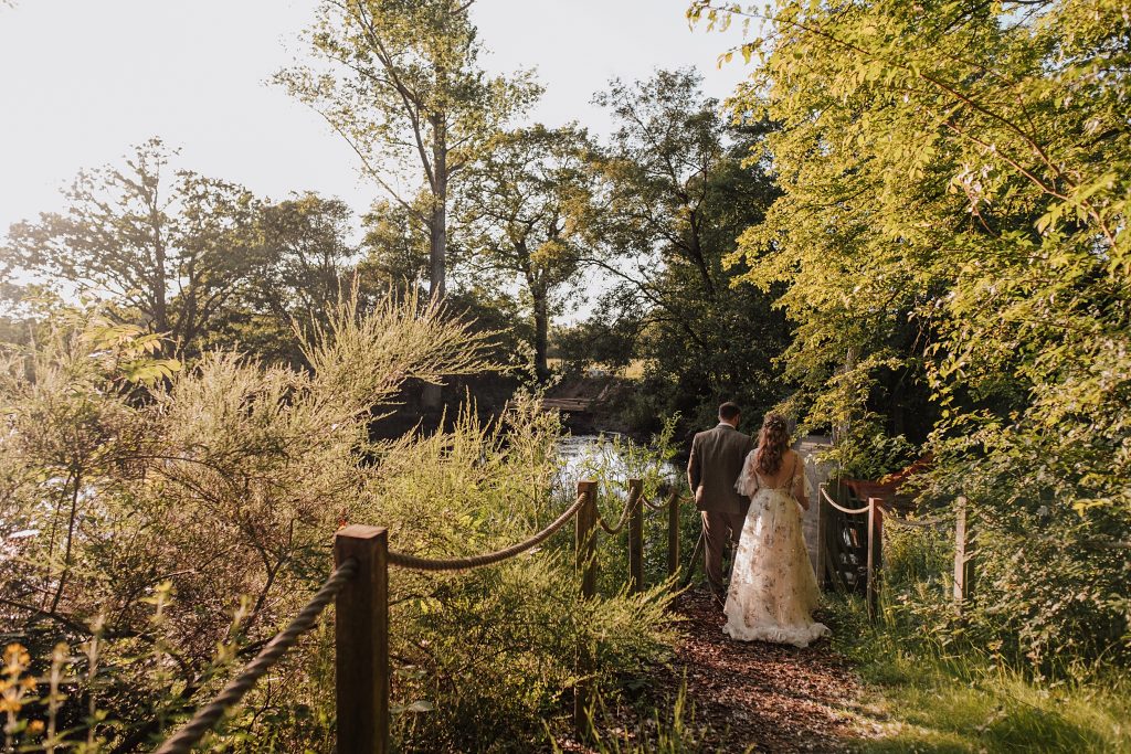 bride and groom walk towards a lake at sunset