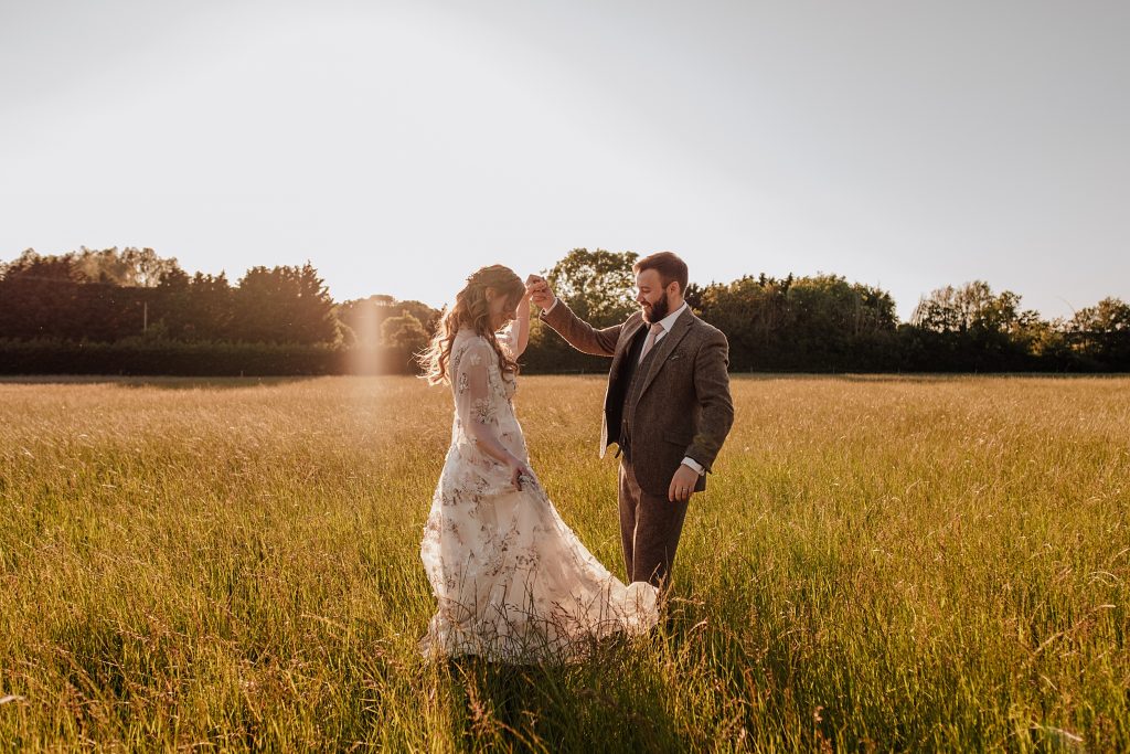 groom twirls his bride in a meadow at sunset