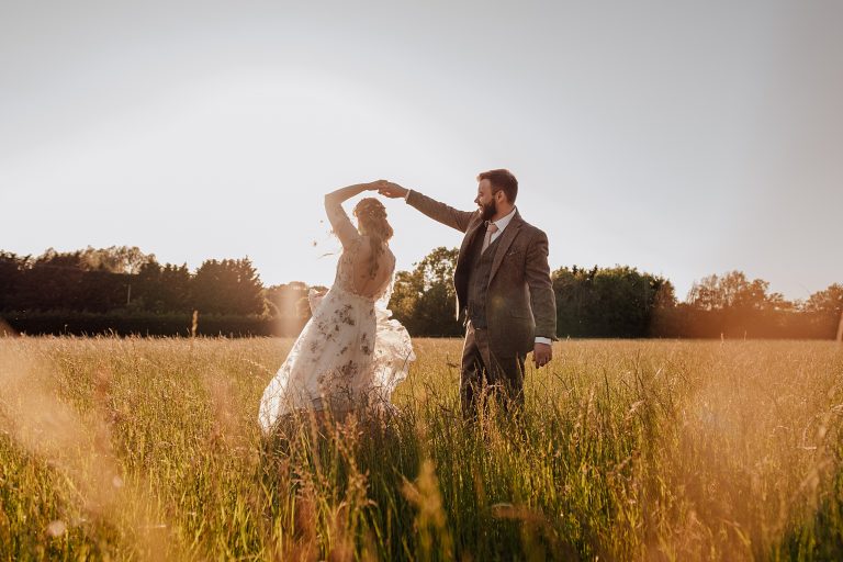 groom twirls his bride in a meadow at sunset