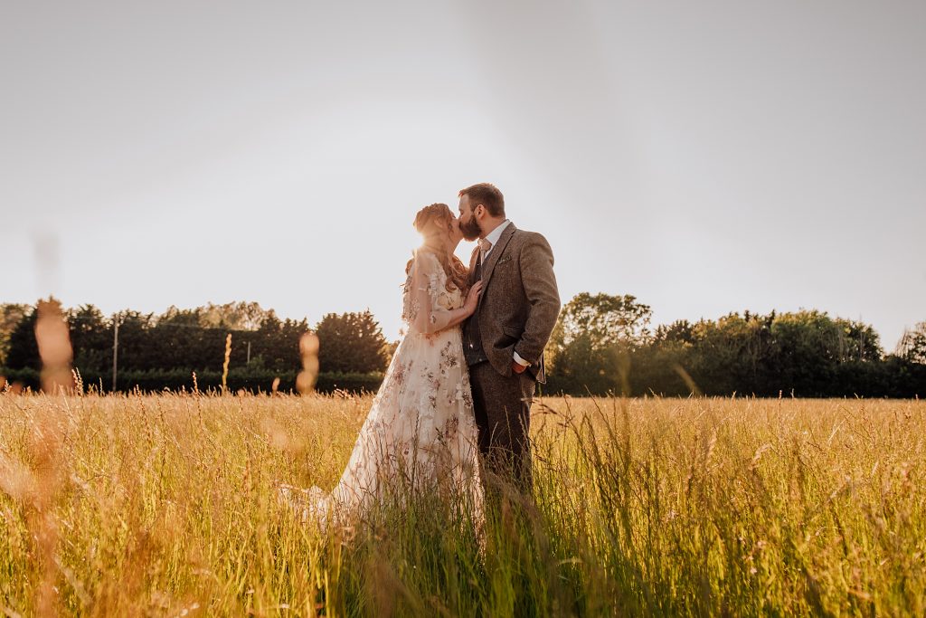 bride and groom kiss in meadow at sunset
