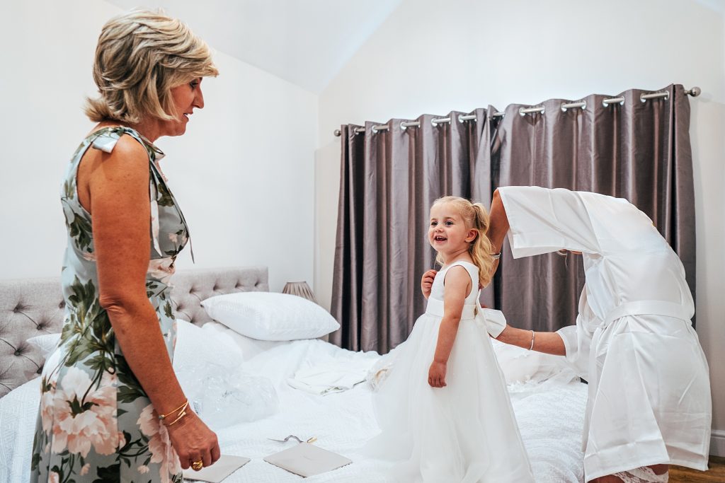 little girl has dress done up on wedding morning watched by grandmother