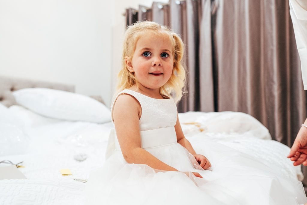little girl in white dress sits on bed