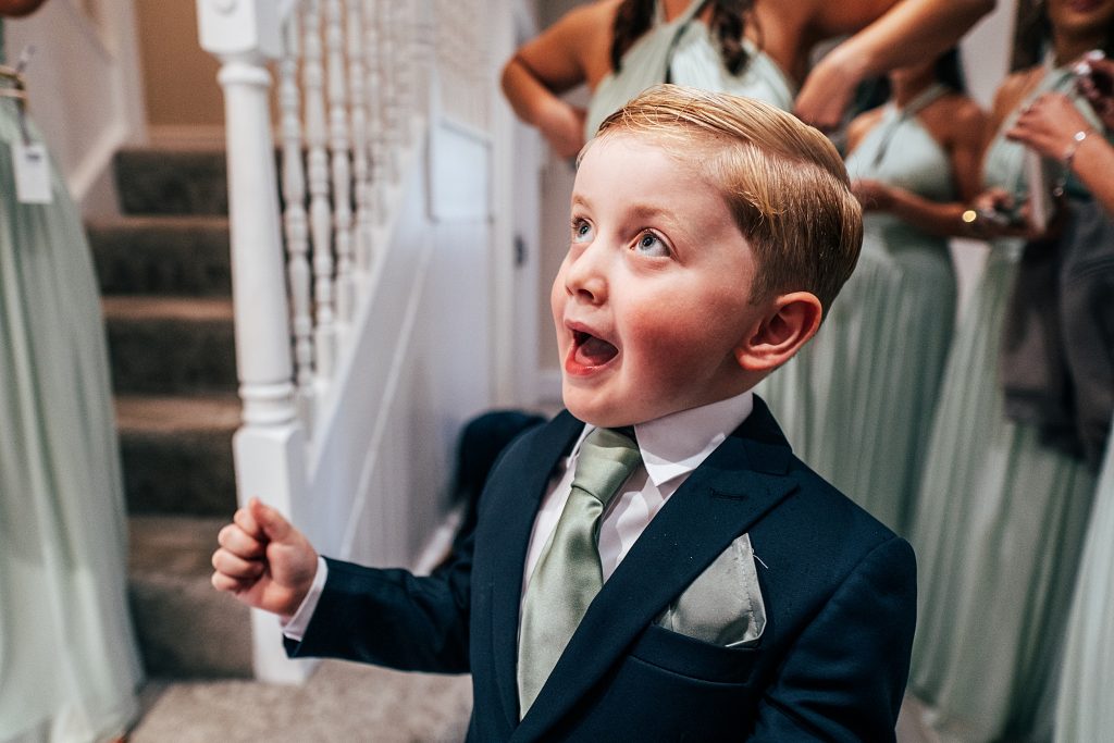 little boy in suit and tie looks up with a wide eyed surprise at his mum in wedding gown