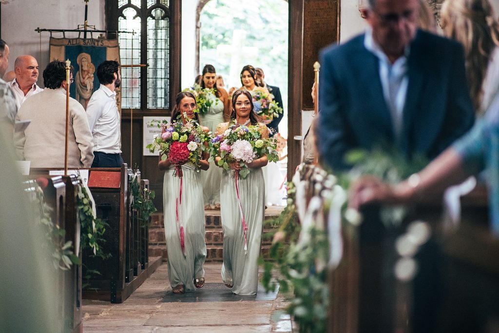 bridesmaids carrying huge bouquets walk down aisle in church