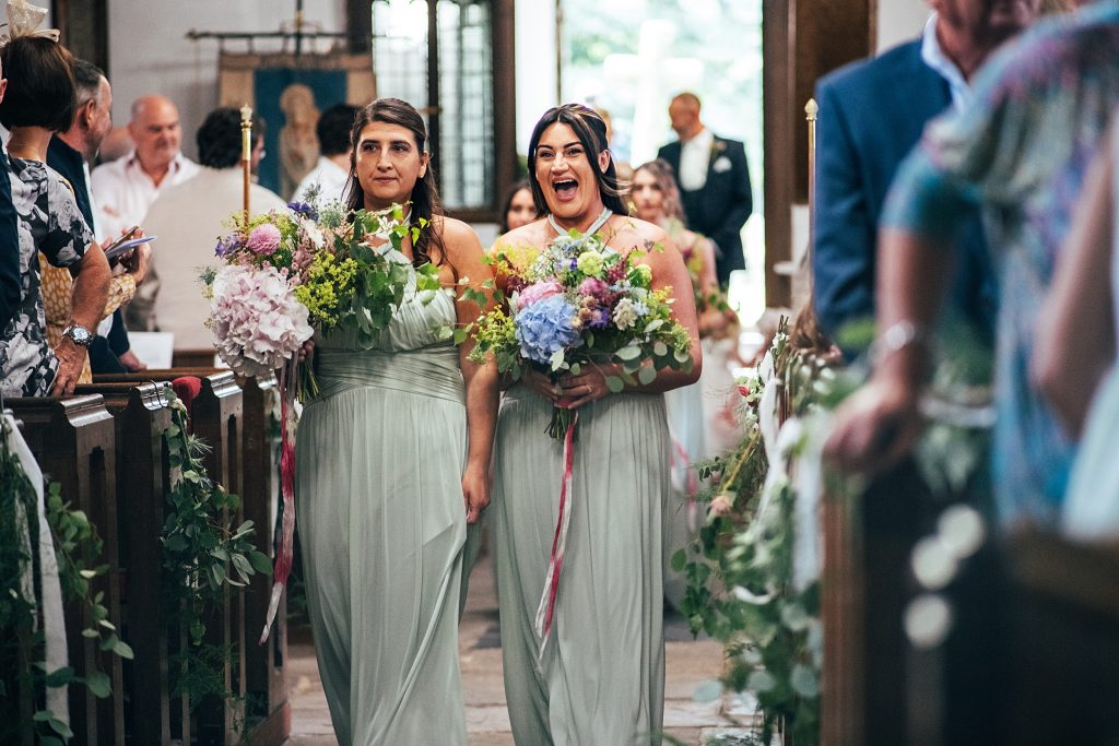 laughing bridesmaids walk down aisle in church