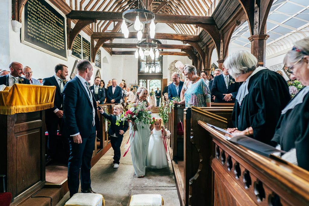 bridesmaid walks page boy and flower girl down aisle in church