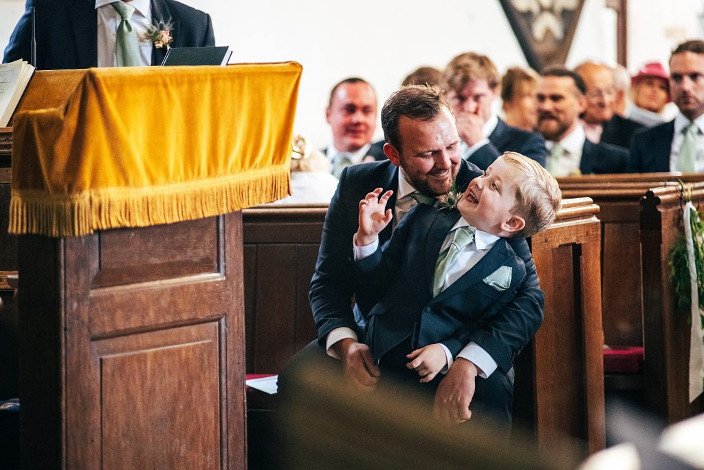 best man makes page boy laugh as he sits on his lap in church