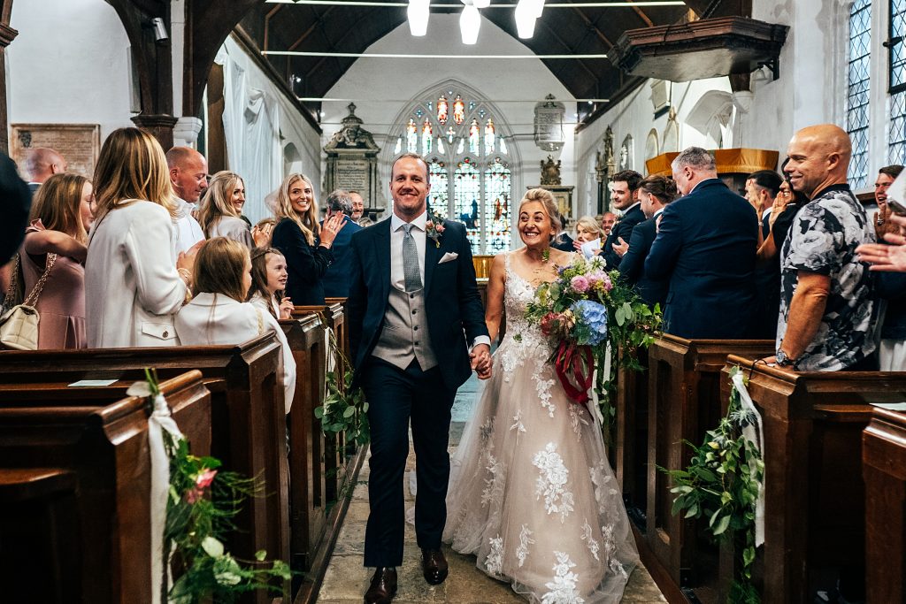 smiling bride and groom walk up aisle in church