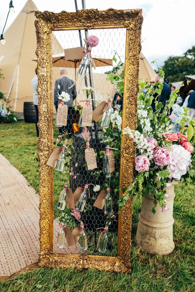 table plan on gold frame with chicken wire, table details on labels handing from flowers in glass bottles