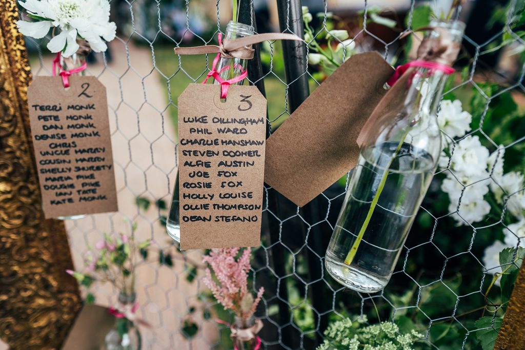 close up of table plans on labels tied round bottle necks holding flowers