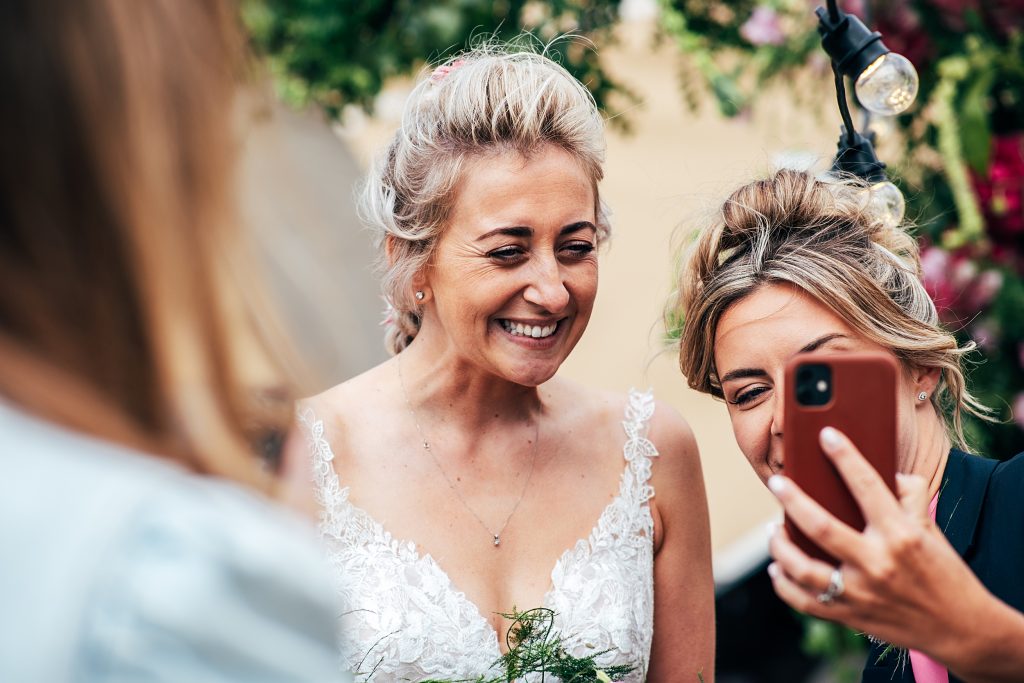 guest shows laughing bride photo on phone