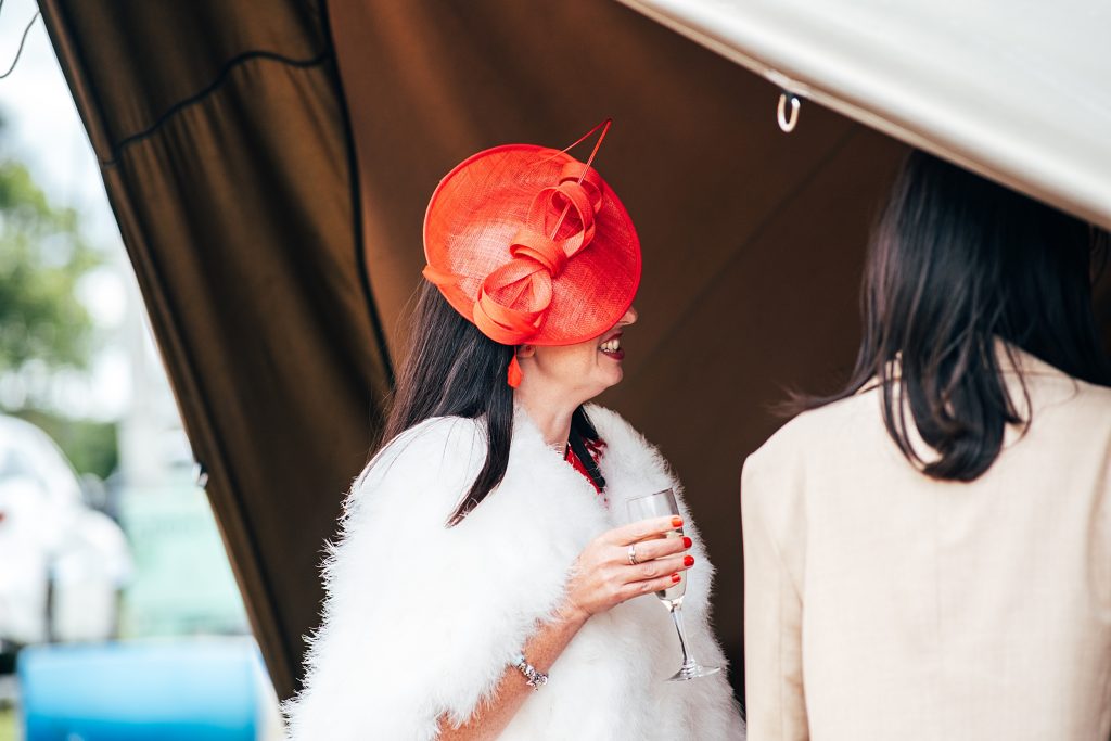 wedding guest in red hat drinks champagne in open sided tipi