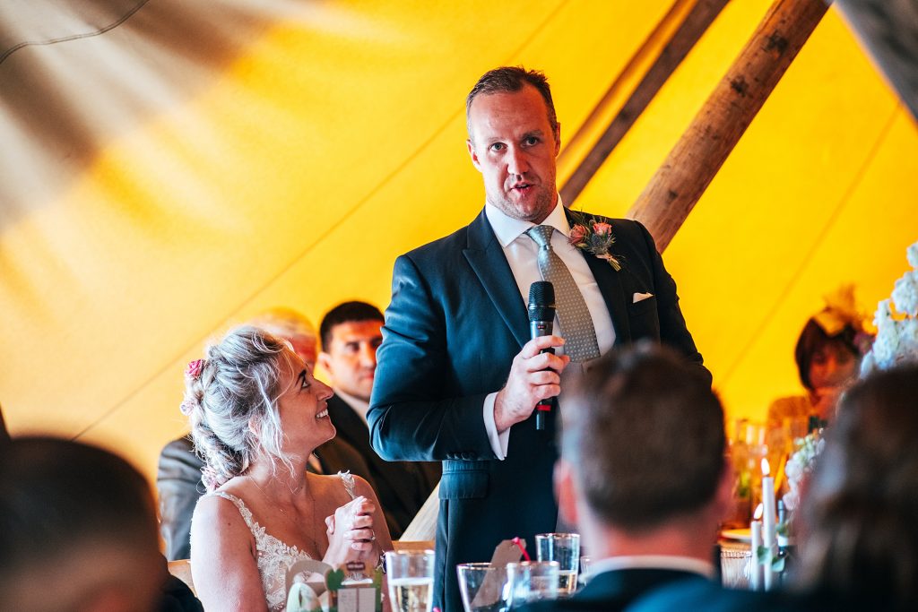 groom gives speech while bride looks up at him in tipi