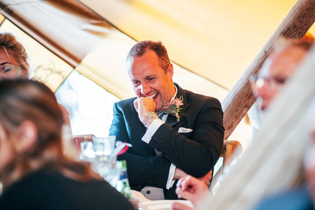 groom puts knuckle to his mouth during best mans speech in tipi