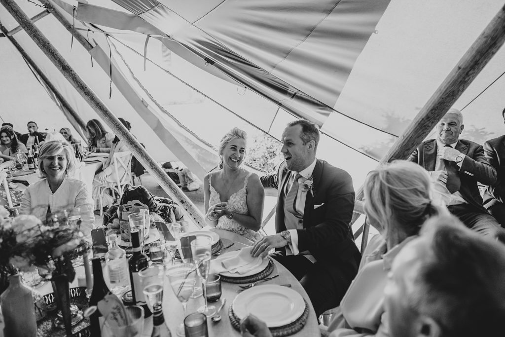 bride and groom laugh at best mans speech in tipi