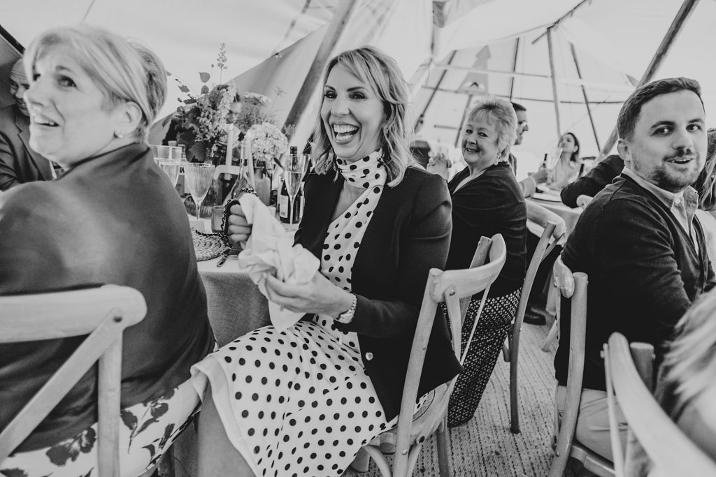 wedding guest in polka dot dress laughs at speeches in tipi