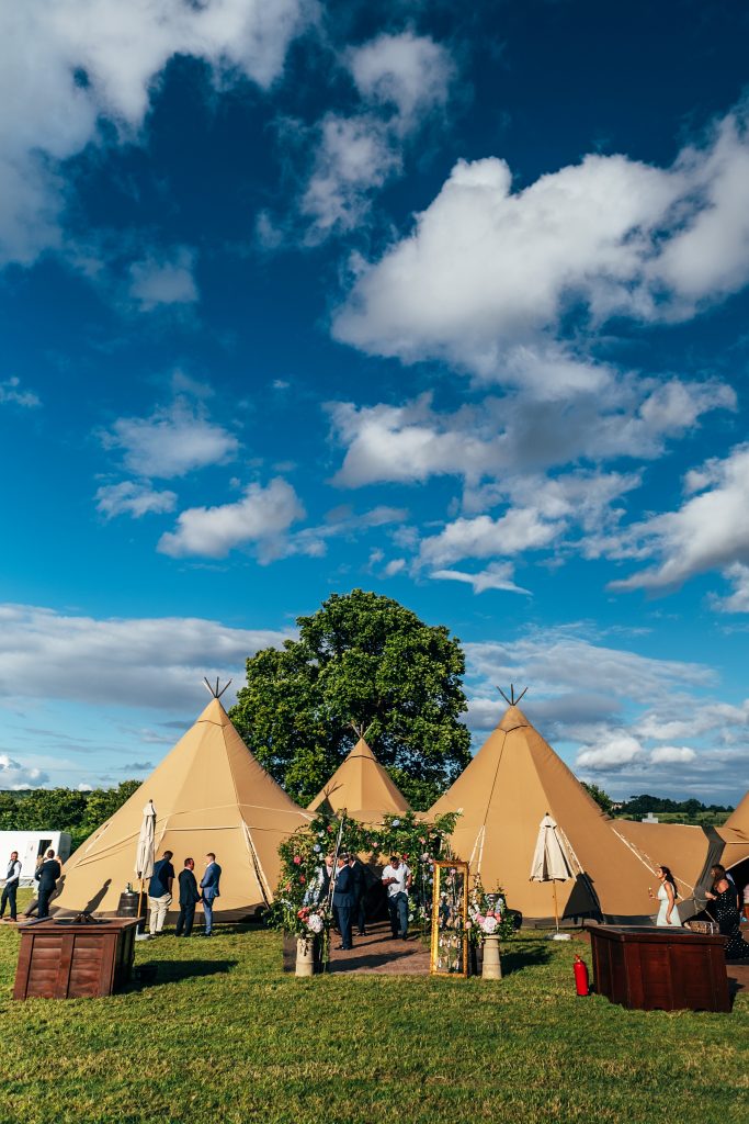 outside view of tipi with wedding guests outside under blue sky with fluffy clouds