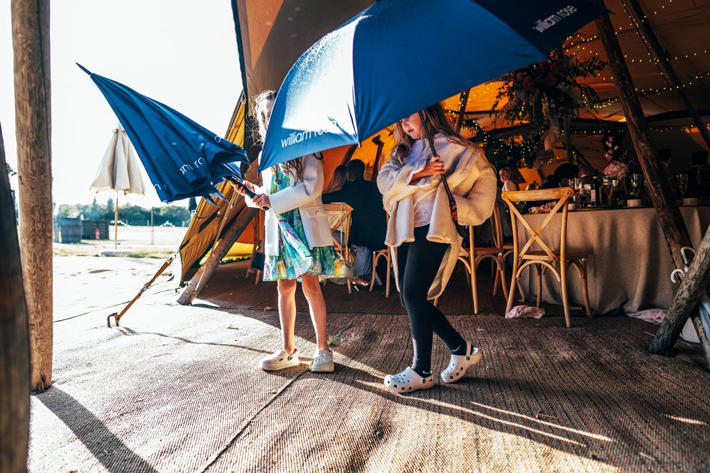 two little girls put up umbrellas as they prepare to exit a tipi in the rain