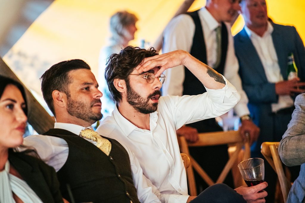 wedding guest hold hand to head as he watches England World Cup game in tipi