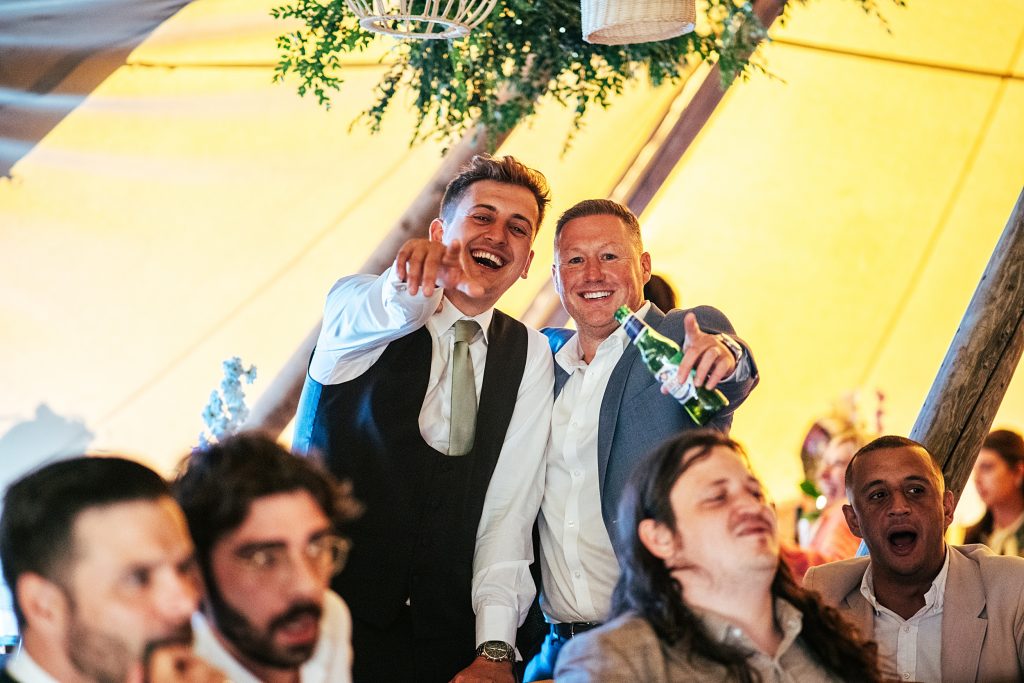 two wedding guests laugh and point at camera